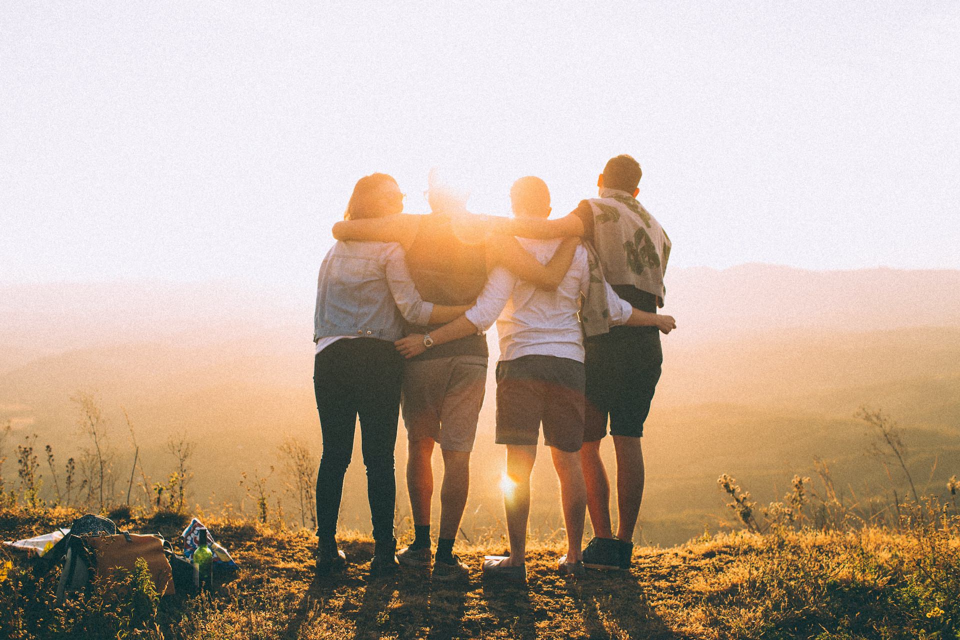 foto de un grupo de cuatro jóvenes en el campo mirando abrazados una puesta de sol