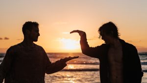 foto atardecer en la playa dos amigos chocando las manos